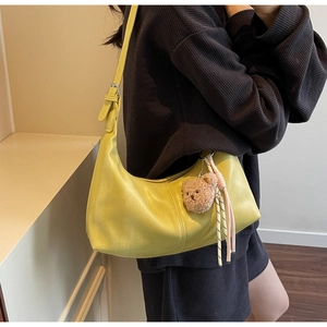 Detail of yellow hobo shoulder bag with plush bear charm and woven keychain