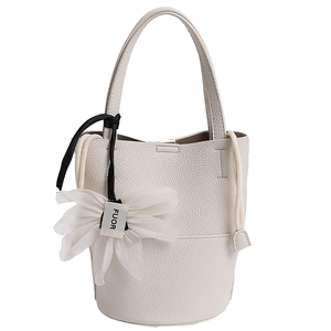 Close-up of white lychee leather bucket bag featuring a floral chiffon charm and drawstring