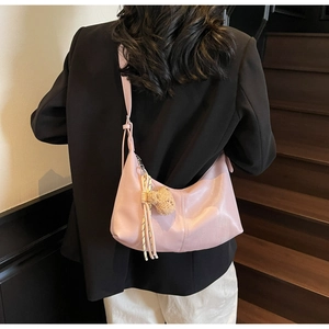 Pink crescent shoulder bag shown with bear charm and colorful rope on a model