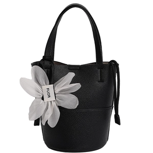 Detail of black pebble grain bucket bag with a white chiffon floral charm and handle