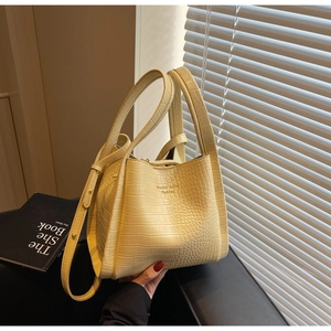 Detail of light yellow crocodile pattern bucket bag with adjustable strap and handles