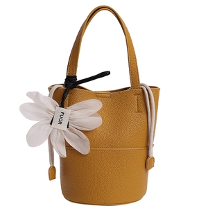 Detail of ginger yellow bucket bag with lychee texture and a white flower charm