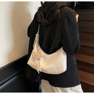 Detail of white half-moon hobo bag with pink bear charm and ribbon on model
