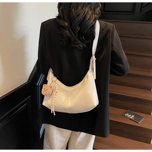 Detail of a creamy white half-moon shoulder bag with a plush bear and silk scarf