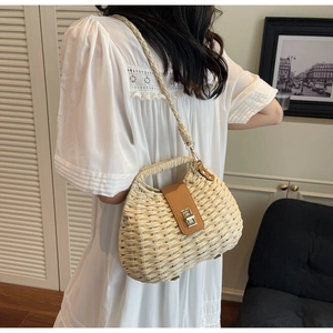 Detail of woven straw handbag with brown leather strap and metal twist lock on model