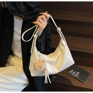 Detail of off-white leather hobo bag with cute plush bear charm and woven tassel detail