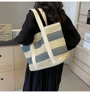 Detail of a large woven straw beach tote featuring navy blue and cream stripes and webbing