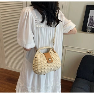 Detail of woven straw bag featuring beige texture, brown leather clasp and woven shoulder strap