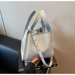 Detail of light blue crocodile-embossed bucket bag showing metal strap buckle and logo
