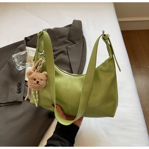 Detail of avocado green leather bag with brown plush bear charm in a lifestyle setting