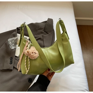 Detail of green leather shoulder bag with plush bear charm on white bedding backdrop