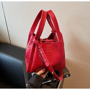 Detail of red crocodile pattern handbag with dual handles and adjustable shoulder strap