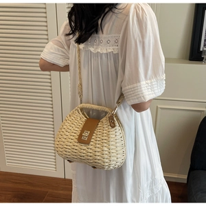 Detail of hand-woven straw crossbody bag featuring brown leather buckle and metal twist lock