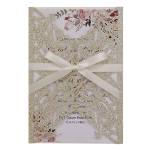 Detailed laser-cut champagne gold glitter wedding invitation with white ribbon and floral inlay