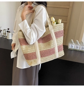 Detail of a large pink and beige striped straw tote bag with wide fabric shoulder strap