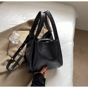 Detail of black crocodile texture bucket bag with sturdy handles and brass hardware