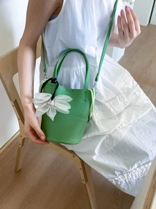Grass green bucket bag in pebble leather with a white flower charm and shoulder strap