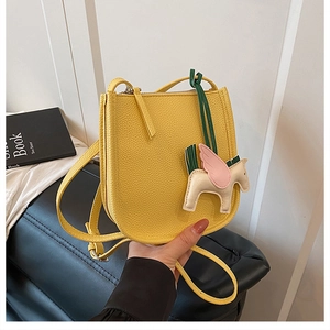 Close-up of yellow pebbled leather handbag featuring a colorful pegasus bag charm and zipper