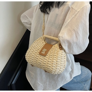 Detailed view of woven straw bag featuring brown leather flap and golden metal lock