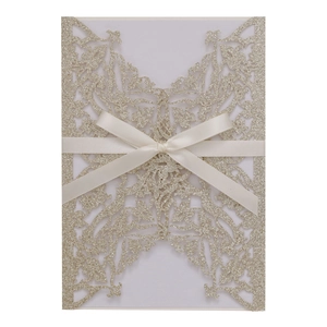 Detailed laser-cut champagne gold glitter invitation cover with a silk ribbon bow