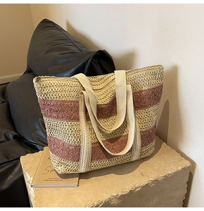 Detail of a striped straw tote bag in beige and rose on a stone base in a modern room