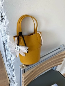 Fashionable bright yellow bucket bag in pebble leather with a white feather pendant