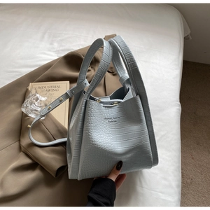 Detail of light blue crocodile texture handbag on brown blazer with shoulder strap