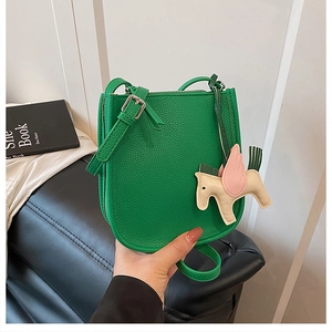 Detail shot of green litchi grain leather bag featuring a colorful horse charm accessory