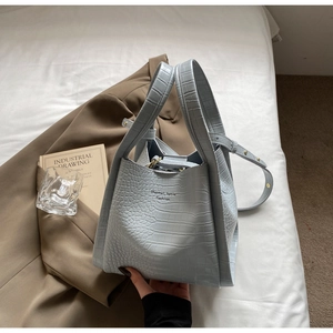 Detail of light blue crocodile embossed handbag with gold hardware and brand logo