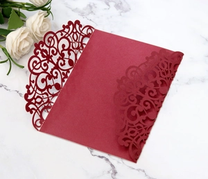Detailed laser-cut scrollwork on burgundy wedding invitation cards atop marble