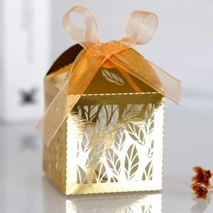 Macro detail of laser-cut gold leaf pattern and chiffon ribbon on a wedding favor box
