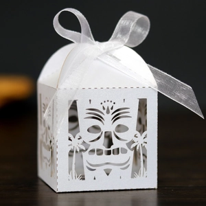 Detail of white laser-cut favor box with Tiki mask pattern and satin ribbon bow