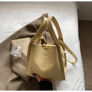 Detail view of cream crocodile-embossed handbag with elegant long strap on white background