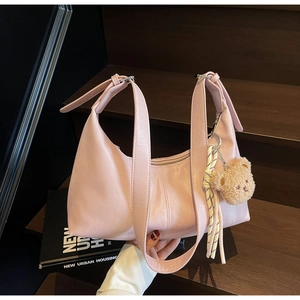 Detail of pink PU leather hobo bag with teddy bear pendant on wooden stairs