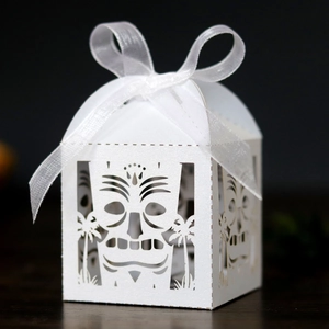 Close-up of white laser-cut favor box featuring Tiki mask patterns and a ribbon bow