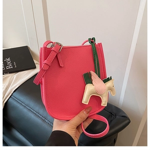 Detail of pink lychee leather crossbody bag featuring a Pegasus charm and slim shoulder strap