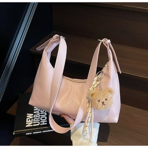 Detail of a soft pink faux leather shoulder bag featuring a cute plush bear pendant accessory