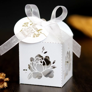 Detail of white laser-cut wedding favor box with organza ribbon and golden thank you tag