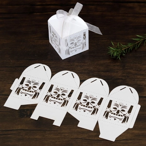 Laser-cut white Tiki mask gift box with organza ribbon on dark wood background