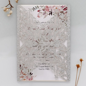 Macro detail of laser-cut silver glitter wedding invitation with watercolor floral insert