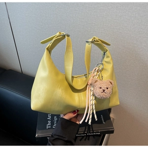 Detail of yellow crescent shoulder bag with teddy bear charm and colorful tassel accent