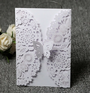 Close-up of white laser-cut wedding invitation featuring a delicate butterfly clasp detail