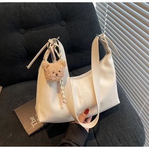 White faux leather hobo bag with a brown teddy bear charm on a striped couch