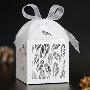 Detail view of laser-cut leaf patterns on white wedding candy box with ribbon