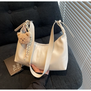 Detailed close-up of cream hobo bag with teddy bear charm and adjustable strap detail
