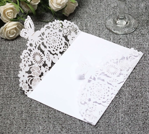 Detail of white laser-cut wedding invitation featuring intricate daisy patterns and butterflies