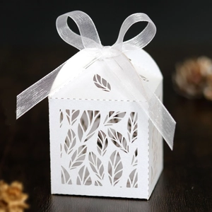 Detailed laser-cut white wedding favor box with hollow leaf pattern and white organza ribbon