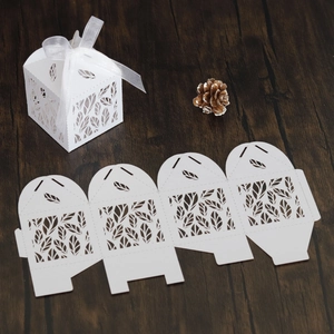 Detailed laser-cut leaf patterns on white cardstock wedding favor box with a silk ribbon