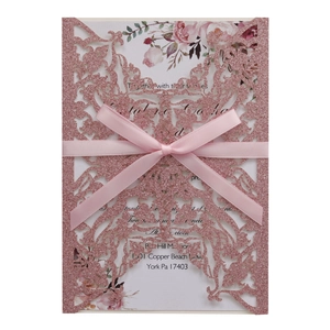 Macro detail of laser-cut glitter paper wedding invitation with pink ribbon bow
