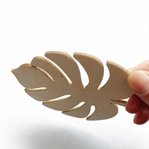 Hand holding a monstera leaf shaped wooden coaster made of laser-cut natural wood
